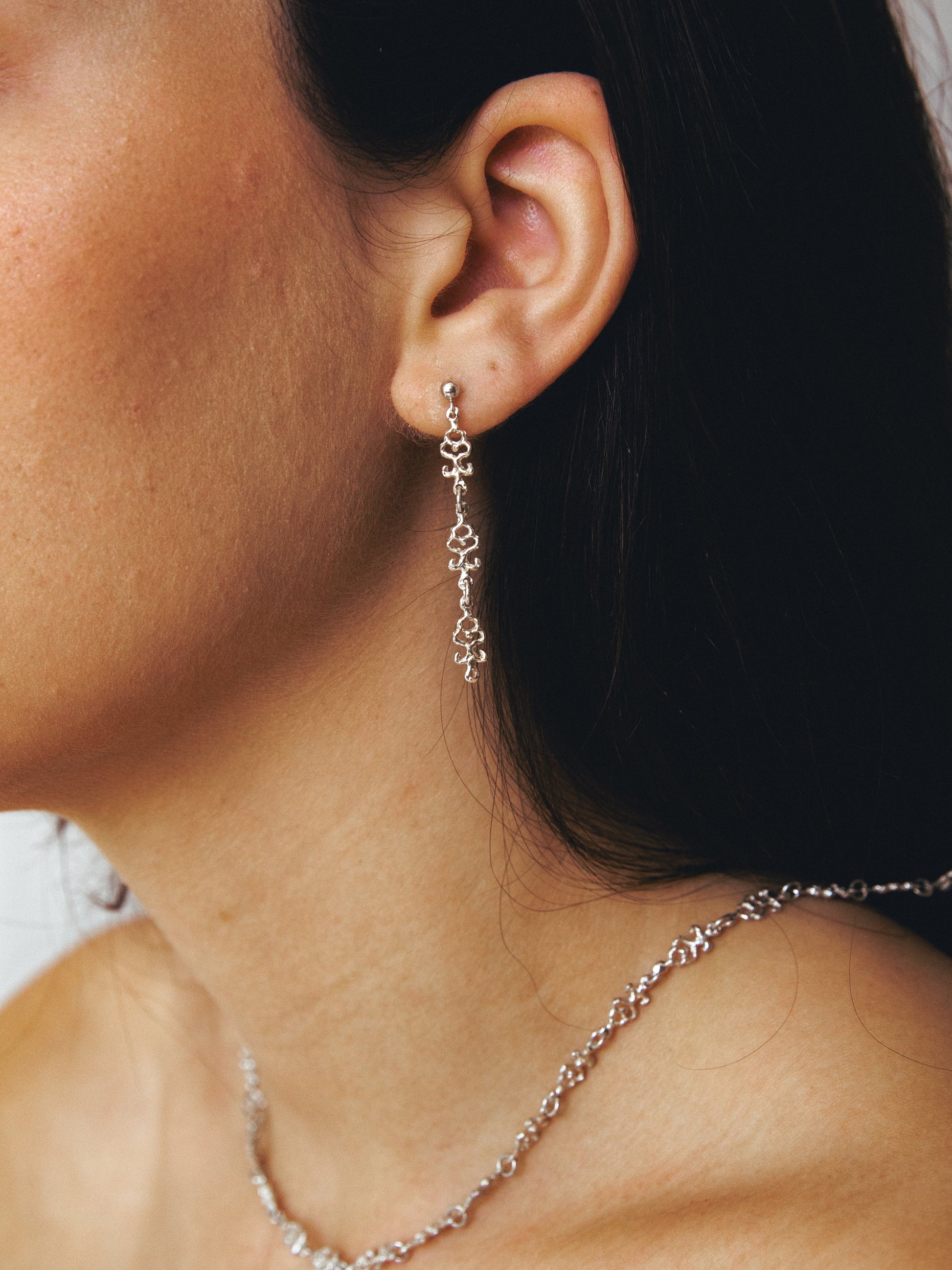 Close-up of a person wearing an handmade silver  dangle earring and necklace.