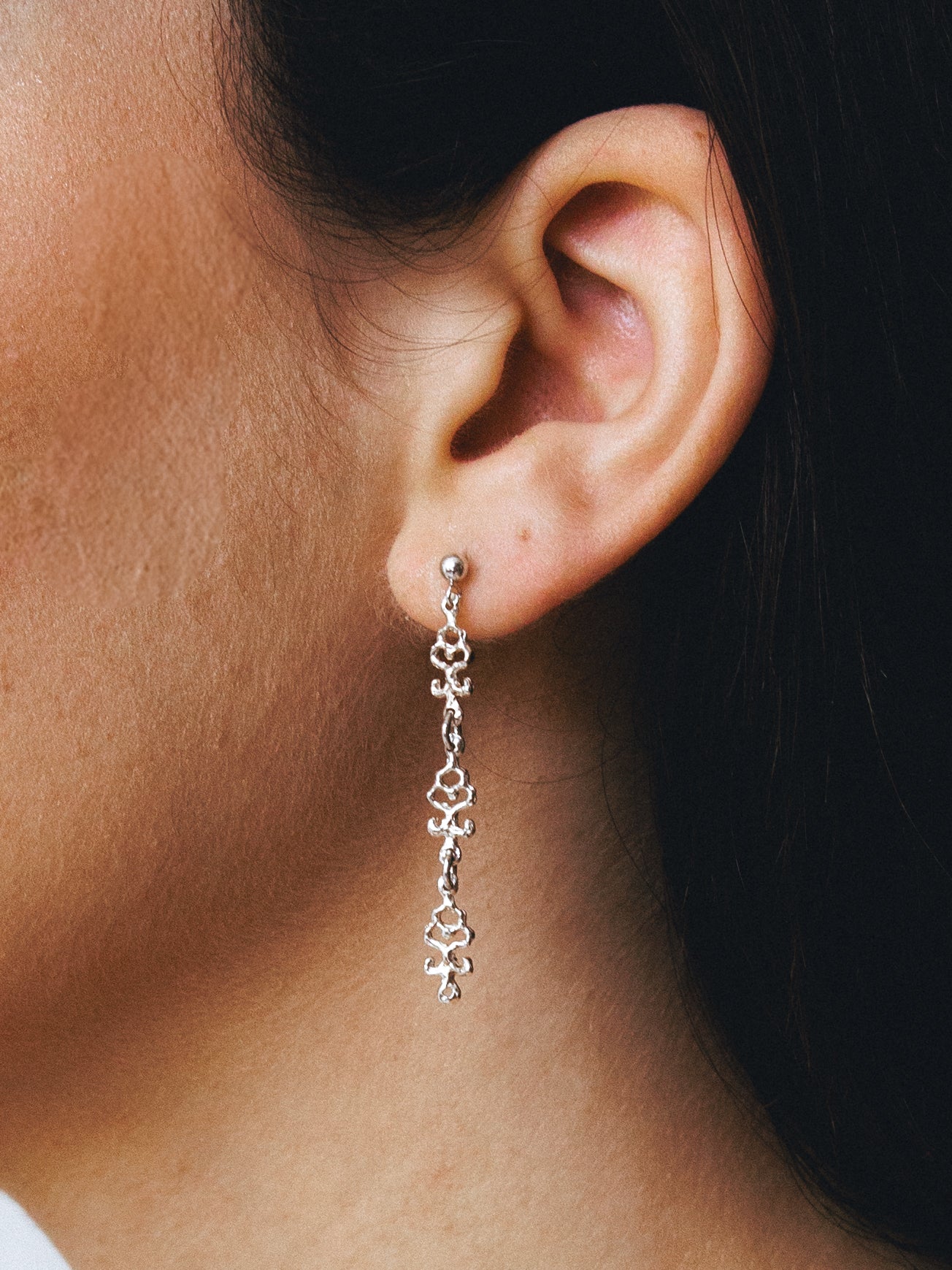 Close-up of an ear wearing an handmade silver earring with a dark background