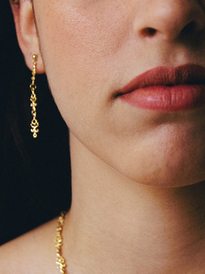 Close-up of a person wearing a gold necklace and earrings against a dark background