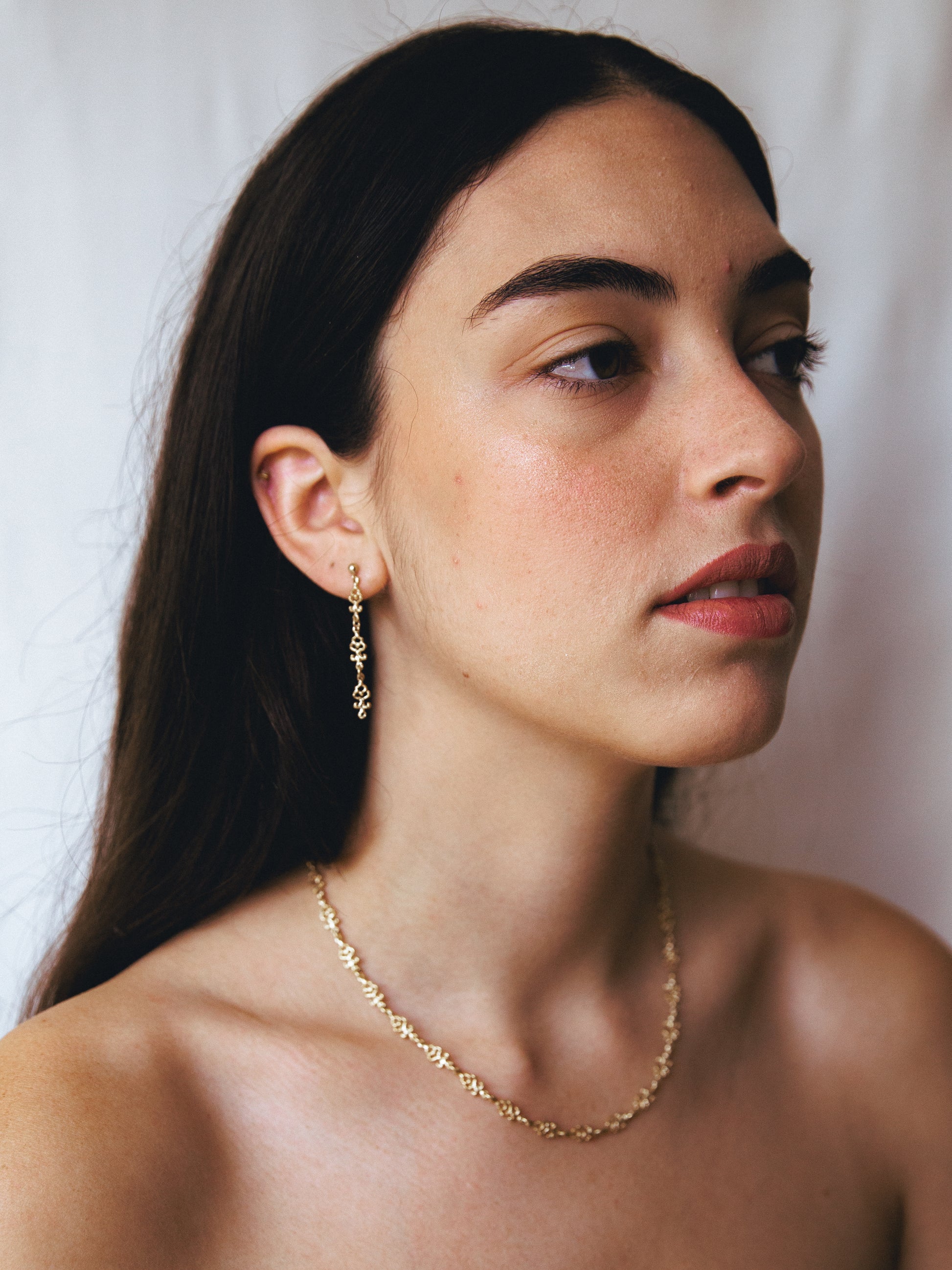 Woman wearing handmade gold 
 dangle earrings and necklace against a white background