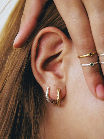Close-up of an ear with gold hoop earrings and a hand wearing rings.