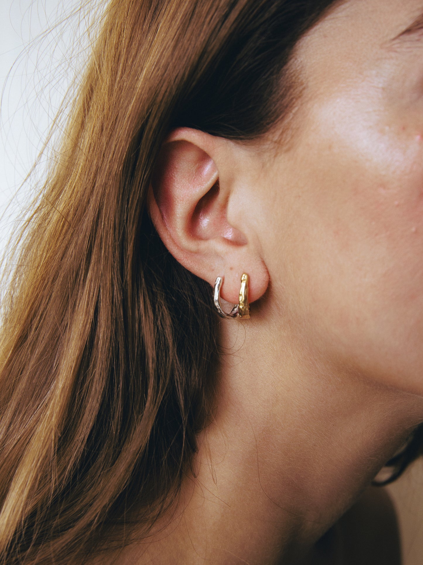 Close-up of a person wearing a gold hoop earring with a blurred background