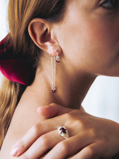 Close-up of a woman wearing a silver earring and ring with a red gemstone.