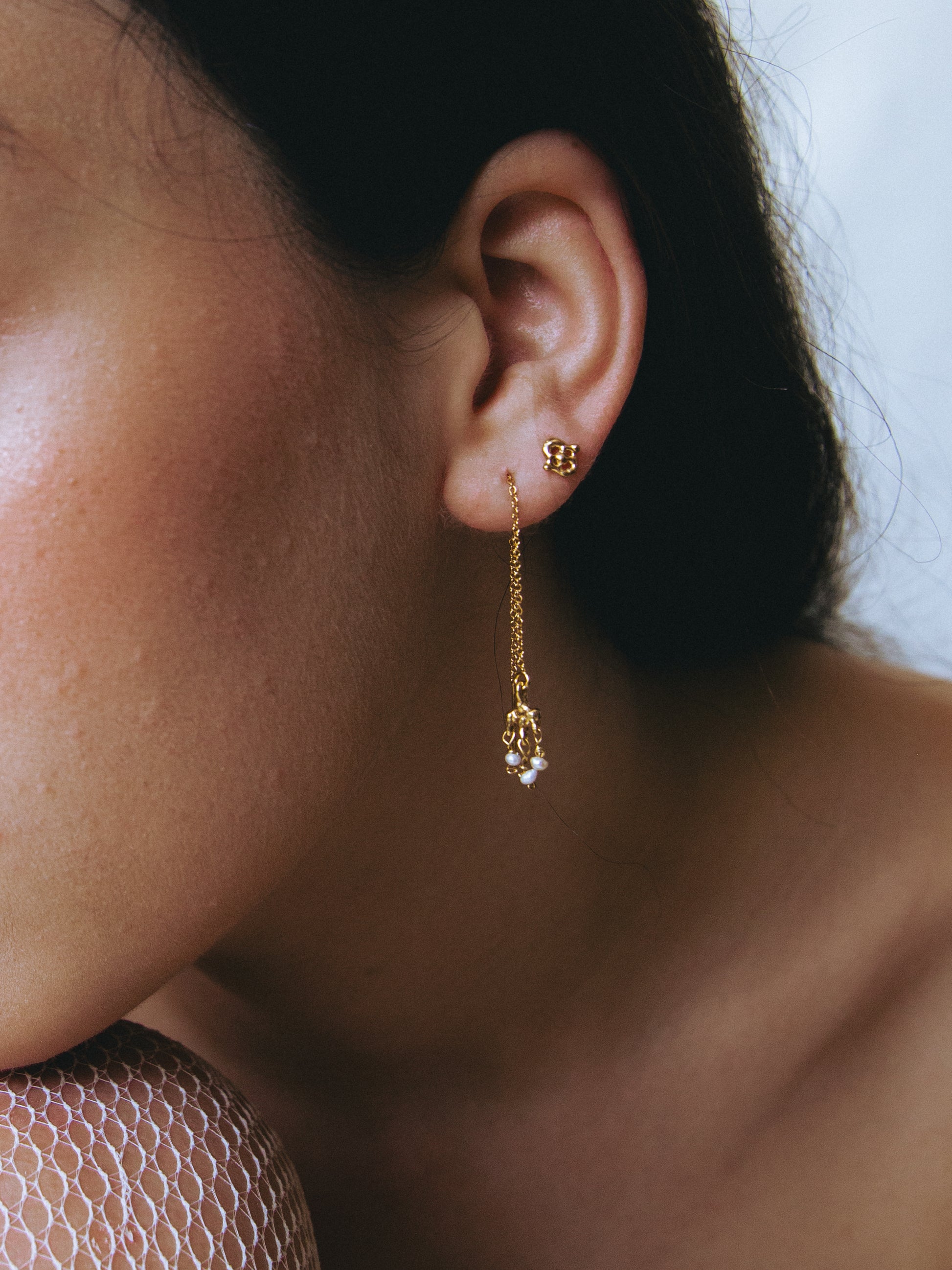 Close-up of a person wearing a gold earring with a pearl drop.