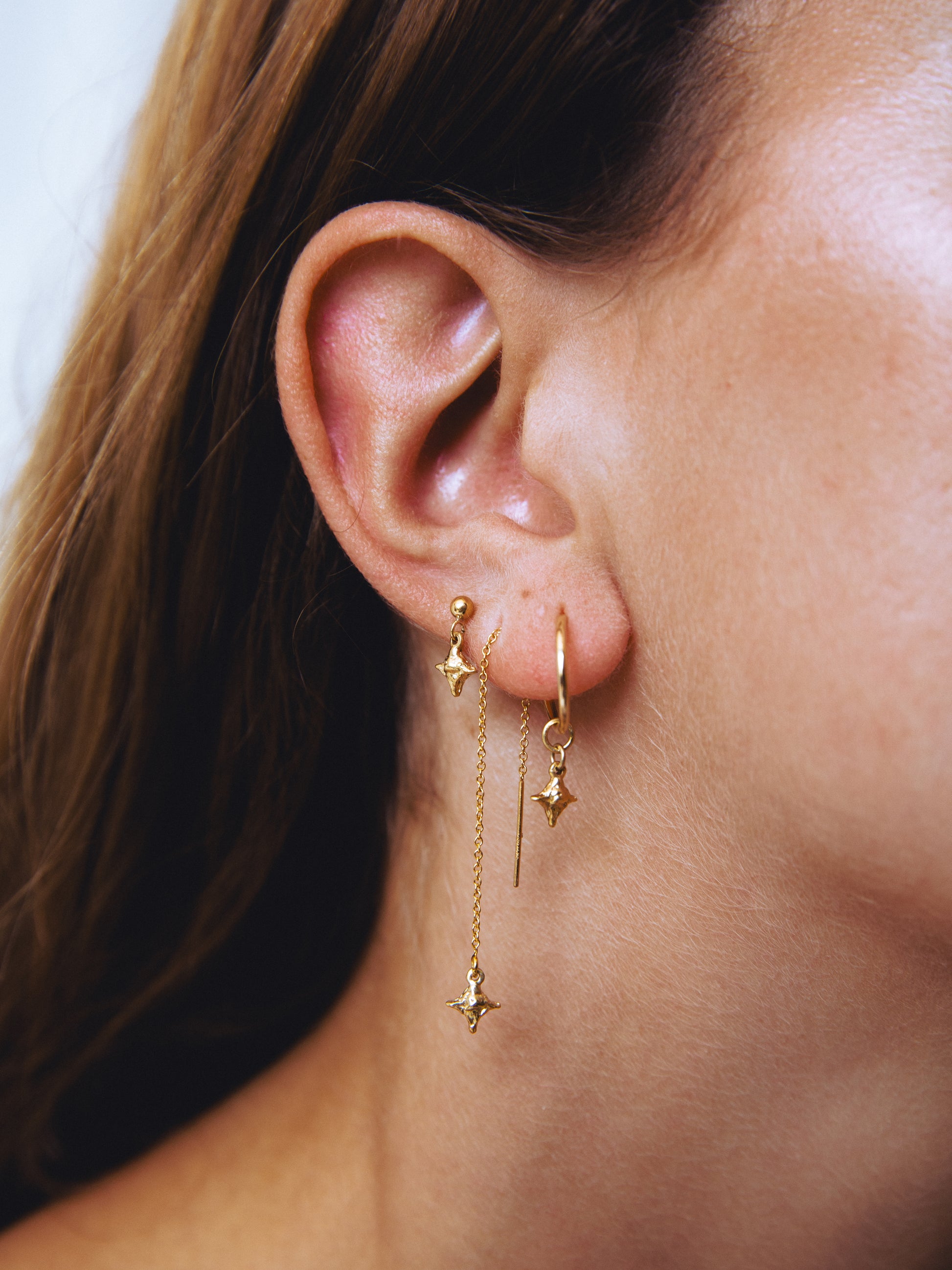 Close-up of an ear wearing gold star-shaped earrings with a blurred background