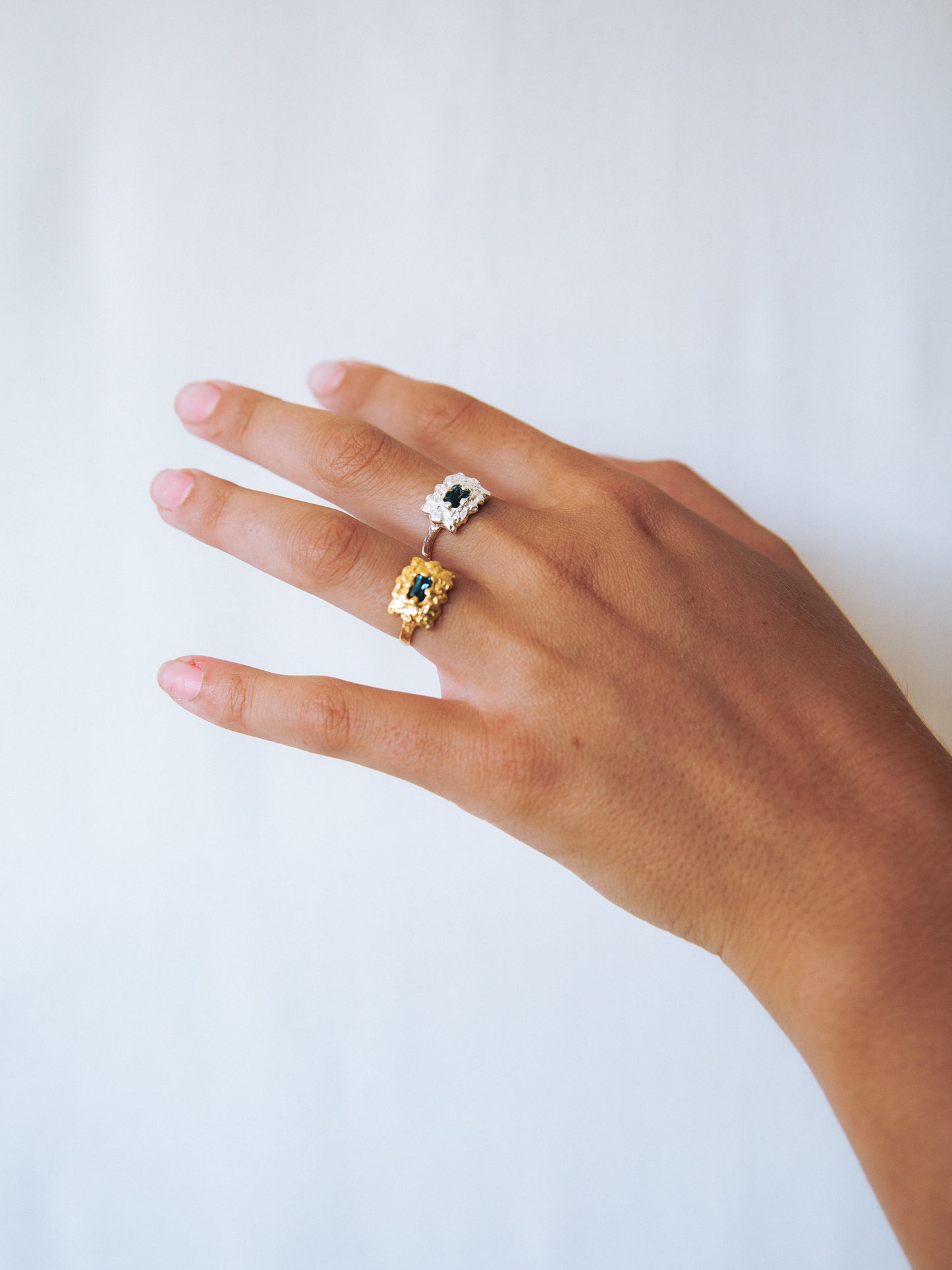 Hand wearing two rings with gemstones on a light background