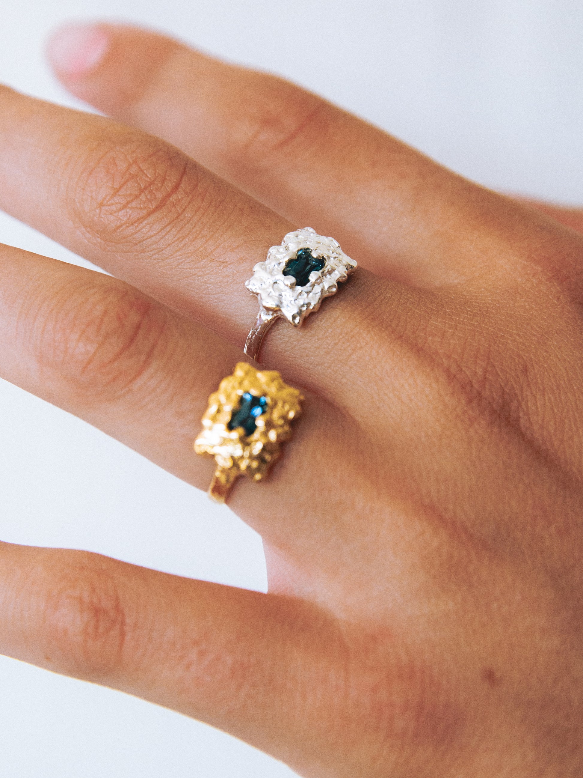 Two rings with gemstones on a hand against a white background