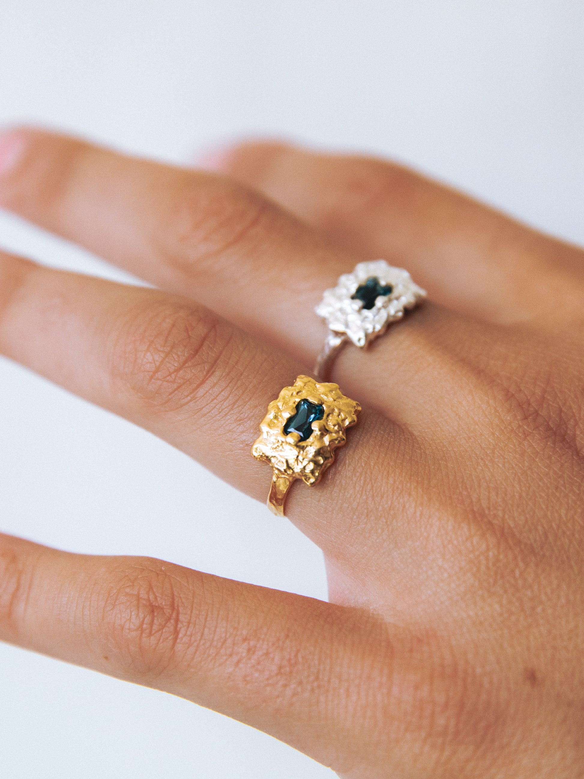Two rings, one gold and one silver, on a person's finger against a white background.