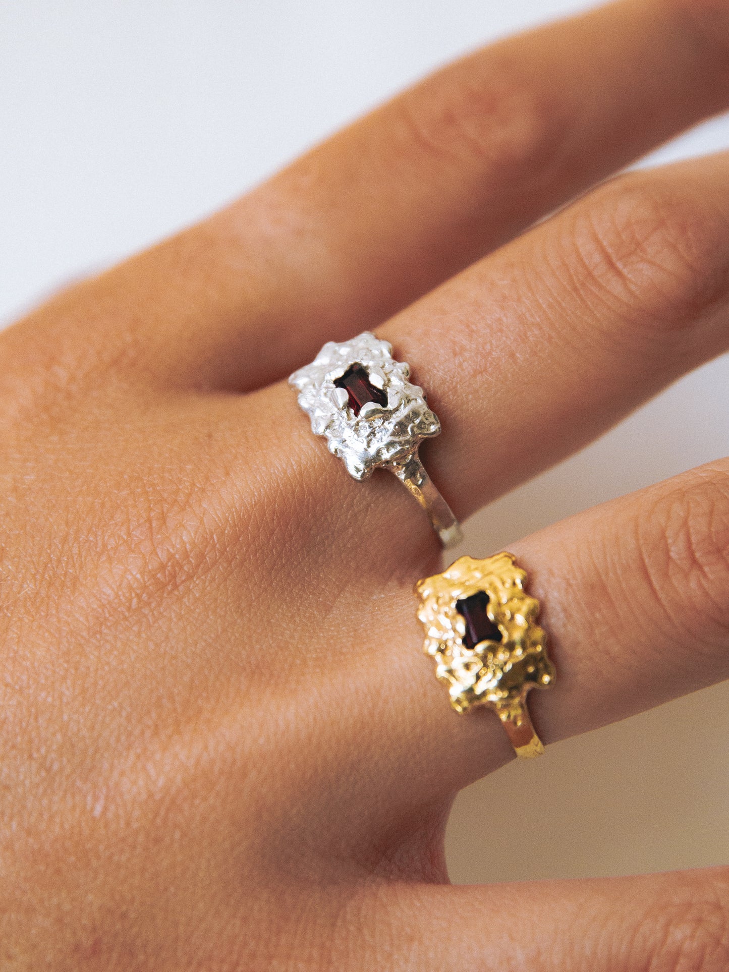 Close-up of a hand wearing two decorative rings on a neutral background