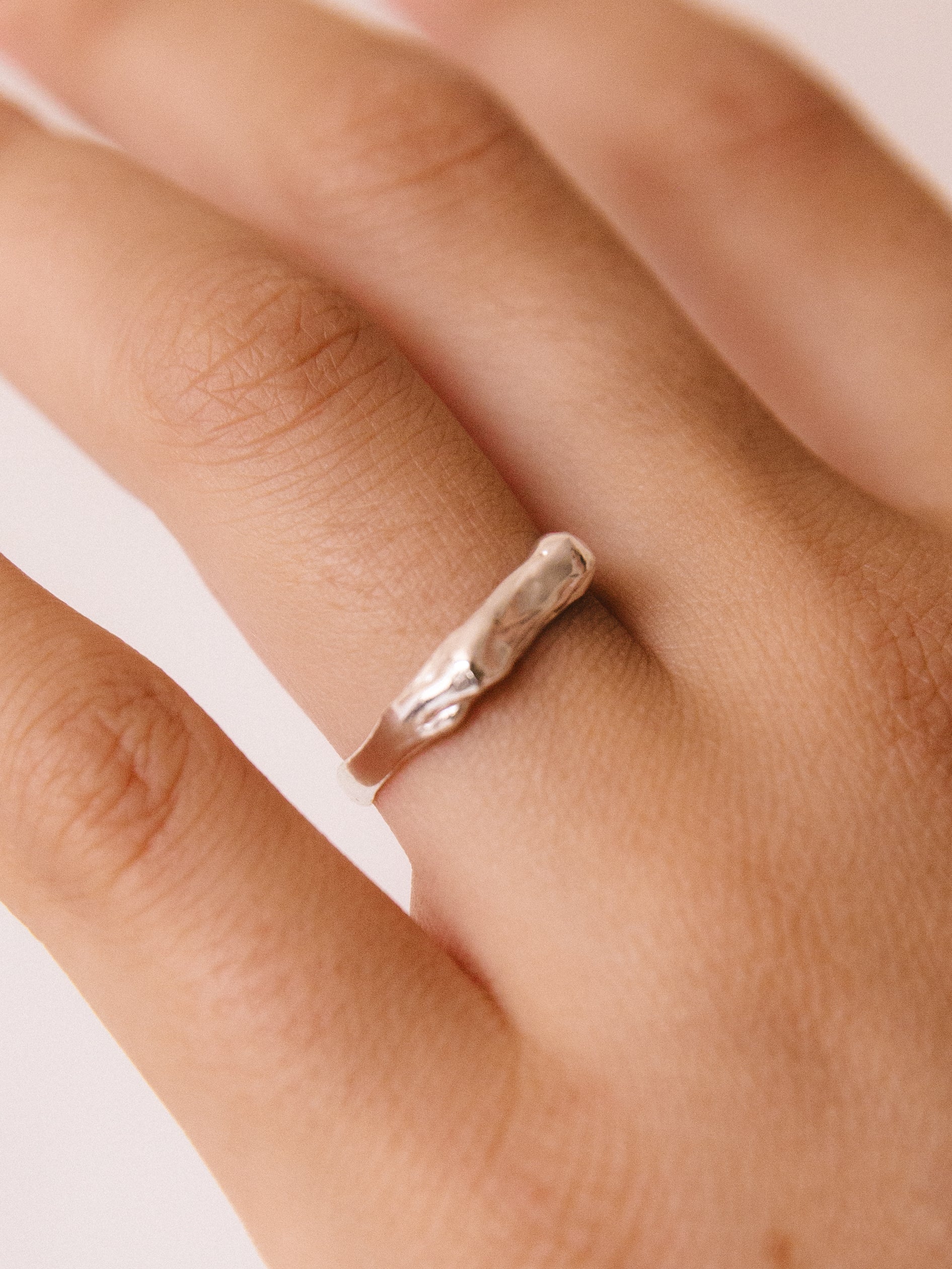 Silver ring on a person's finger with a plain background