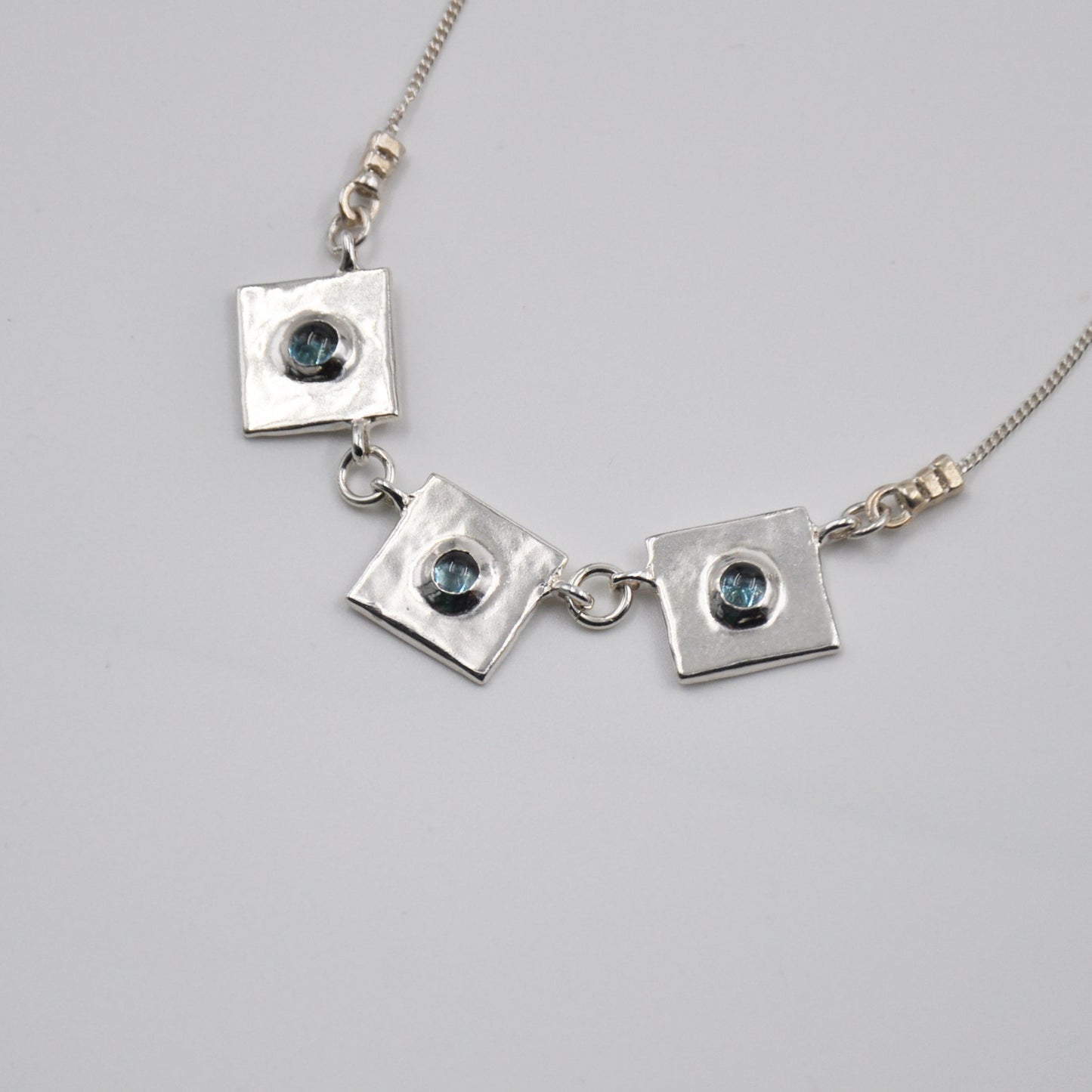 Silver necklace with square pendants on a light gray background