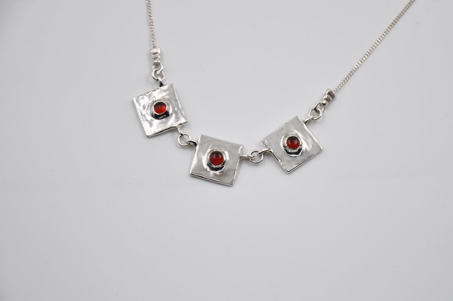 Silver necklace with square pendants and red stones on a light gray background
