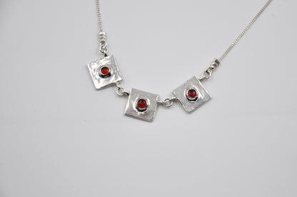 Silver necklace with square pendants and red stones on a light gray background