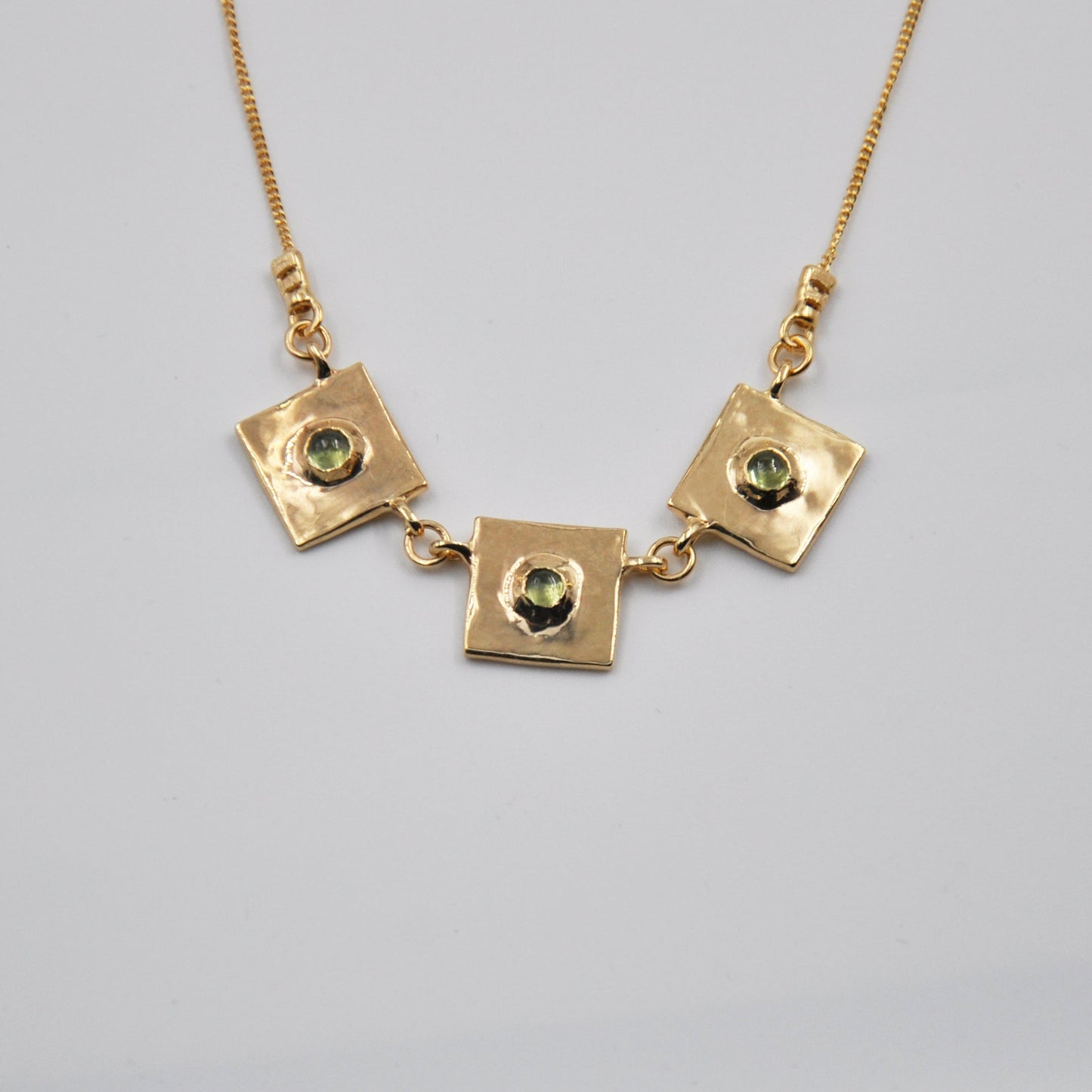 Gold necklace with square pendants on a light gray background