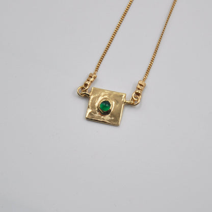 Gold necklace with a square pendant featuring a green gemstone on a light gray background