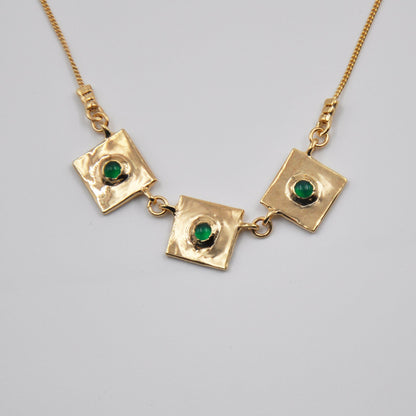 Gold necklace with square pendants and green gemstones on a light gray background