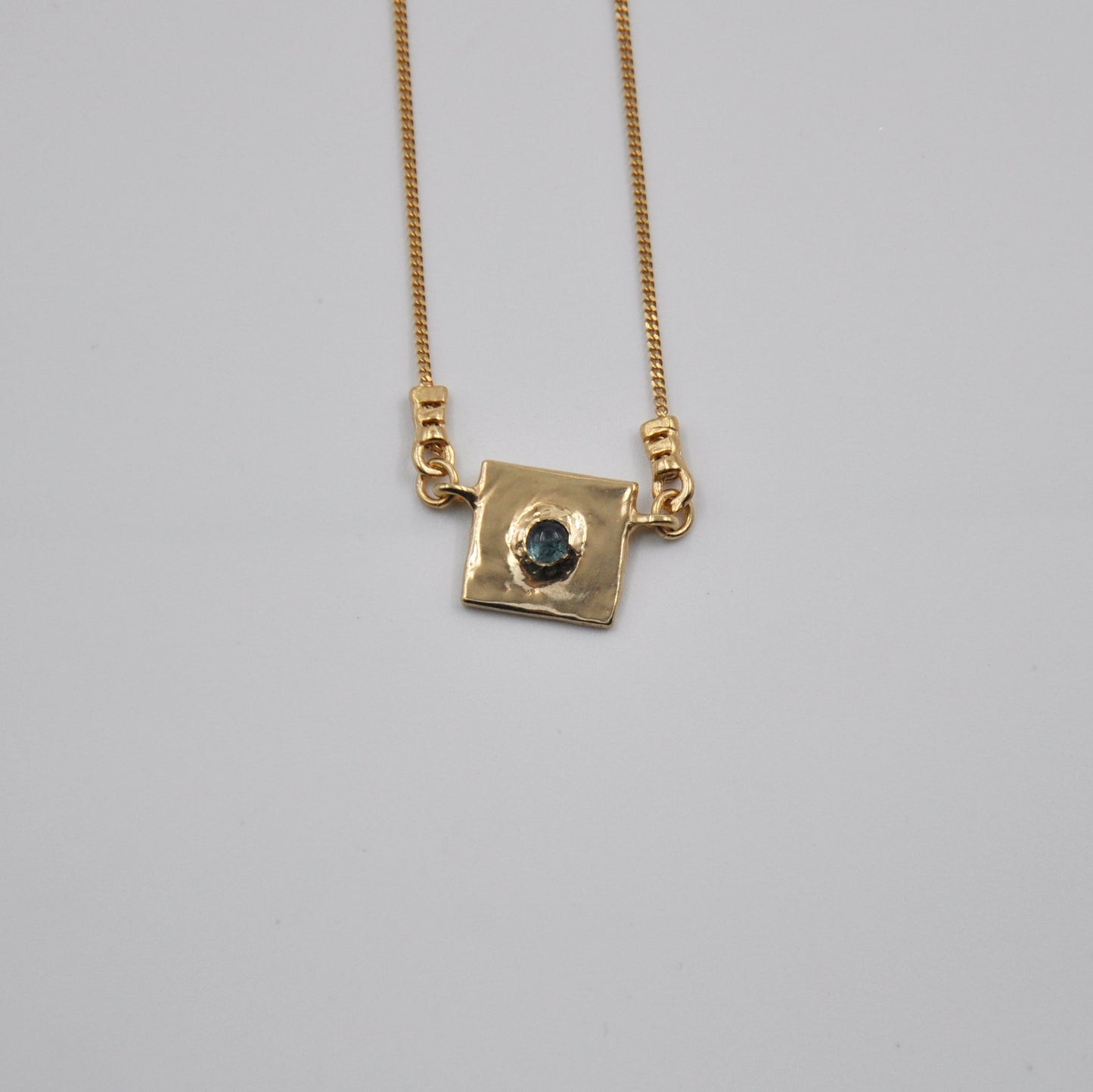 Gold necklace with a square pendant on a gray background