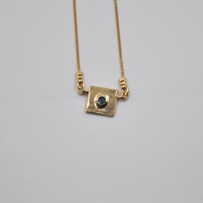 Gold necklace with a square pendant on a gray background