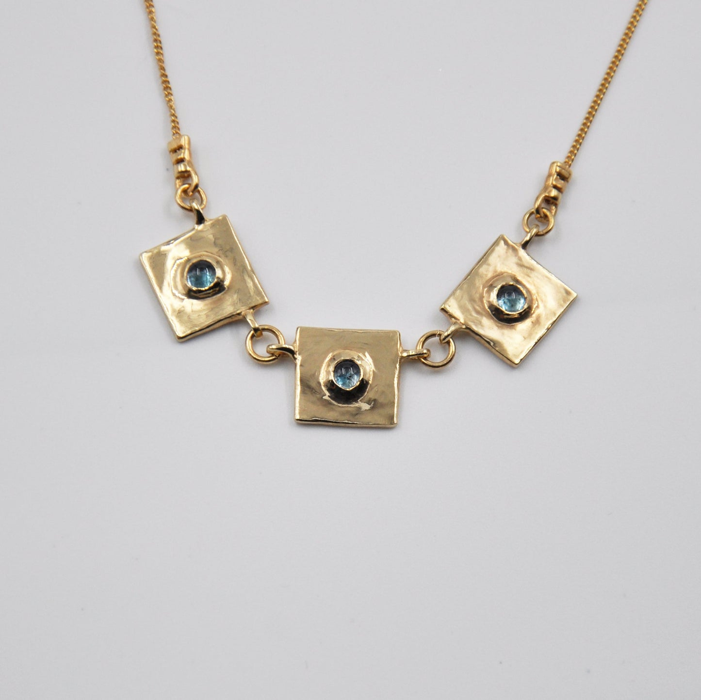 Gold necklace with square pendants and gemstones on a light gray background