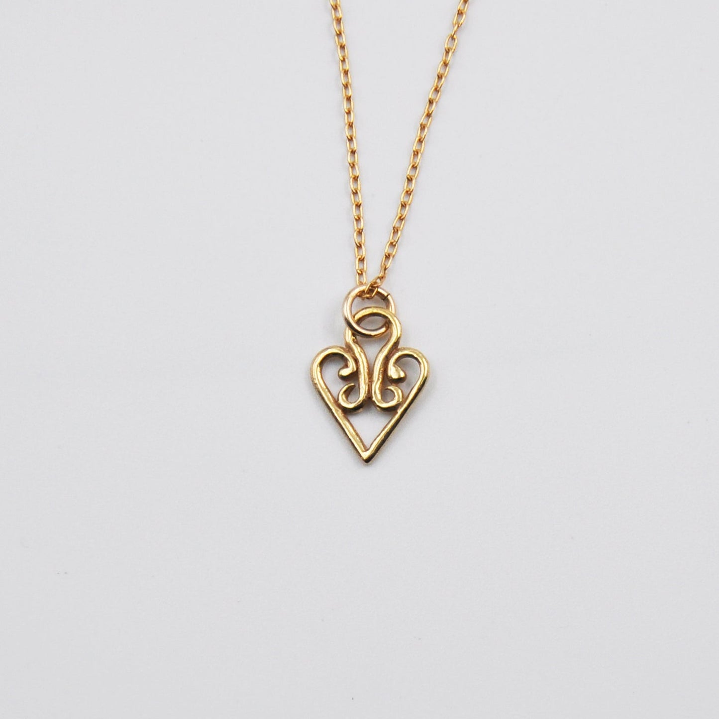 Gold heart-shaped pendant necklace on a light gray background