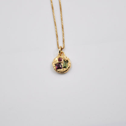 Gold necklace with a pendant featuring gemstones on a light gray background