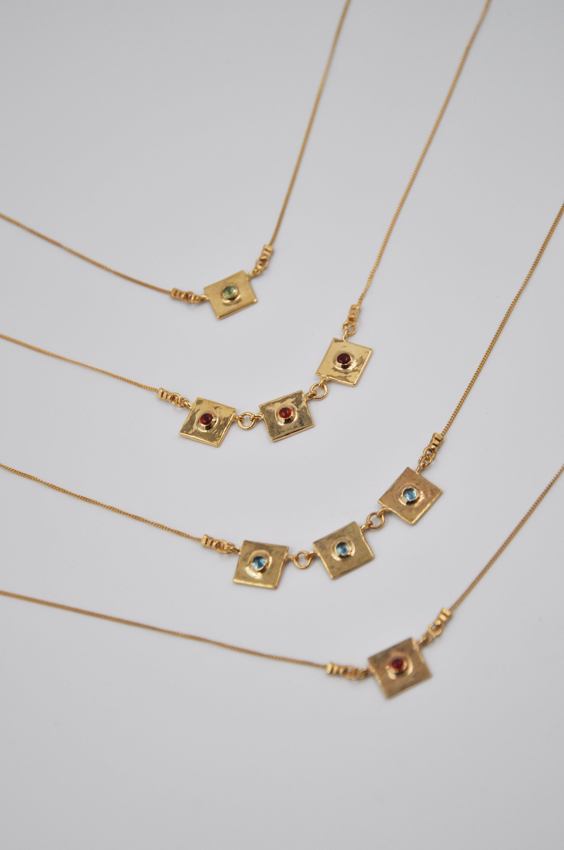 Gold necklaces with square pendants on a light gray background