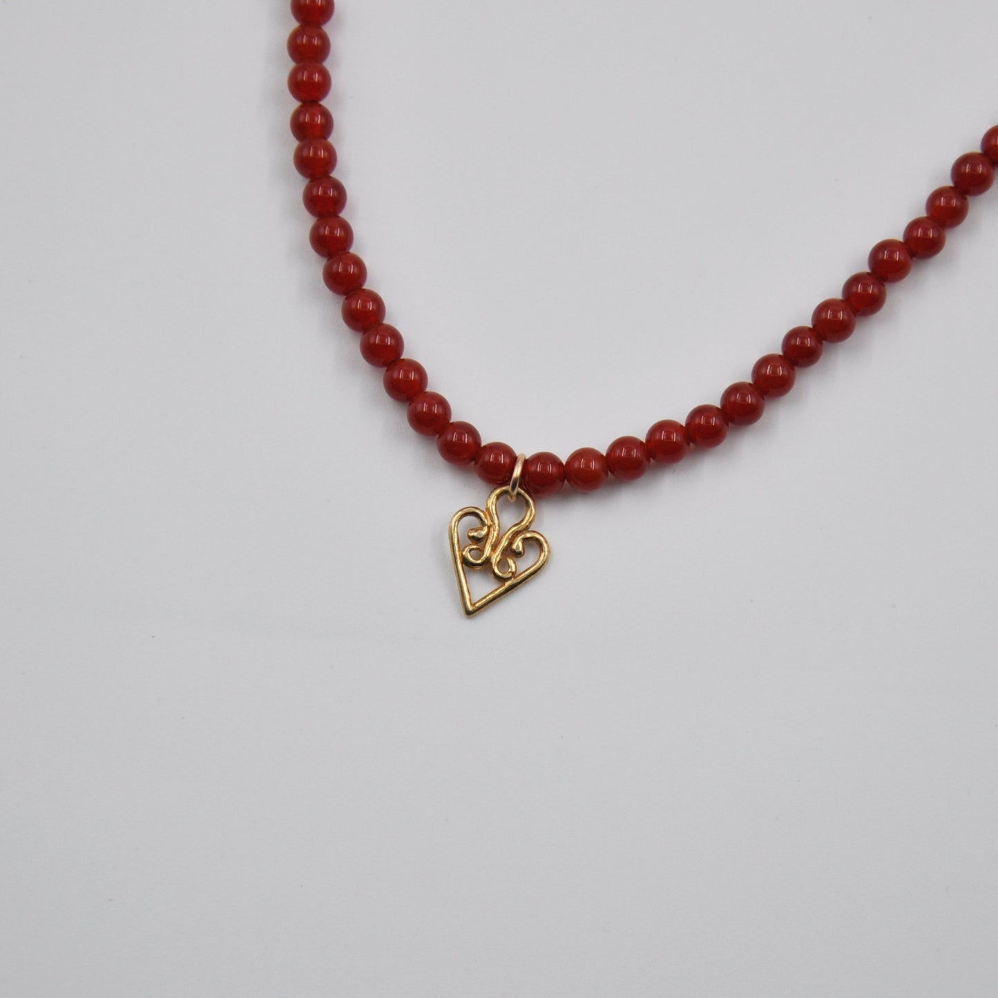 Red beaded necklace with a gold heart-shaped pendant on a light gray background