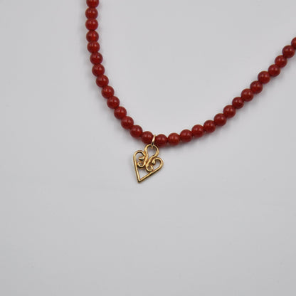 Red beaded necklace with a gold heart-shaped pendant on a light gray background