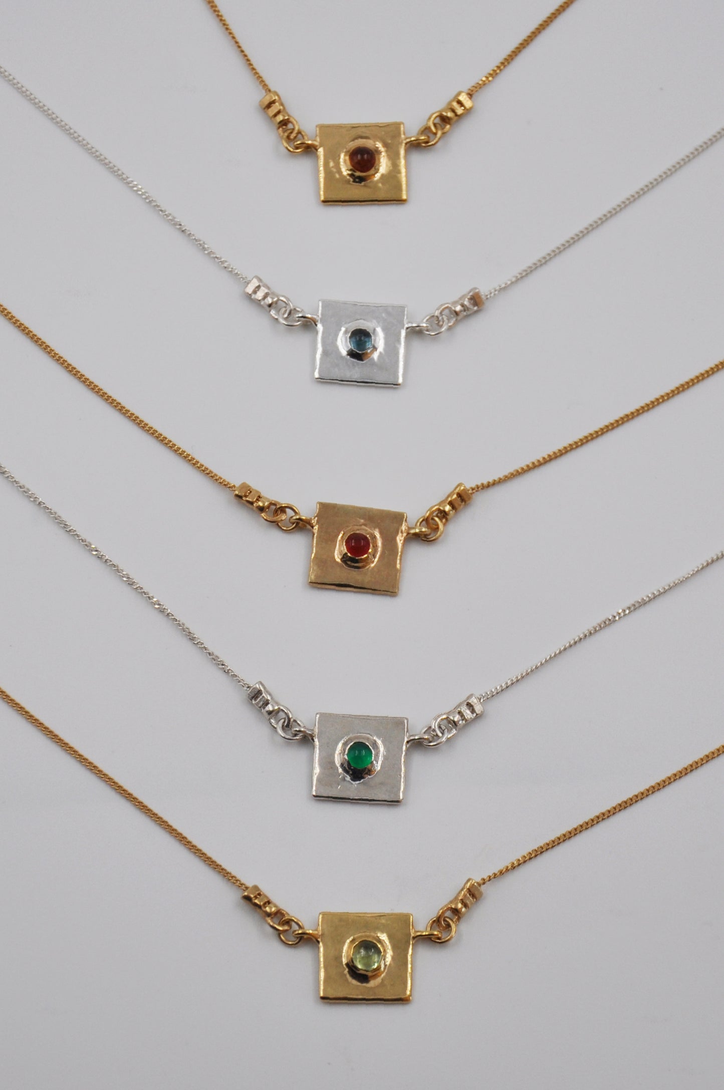 Set of gold and silver necklaces with gemstone pendants on a light gray background