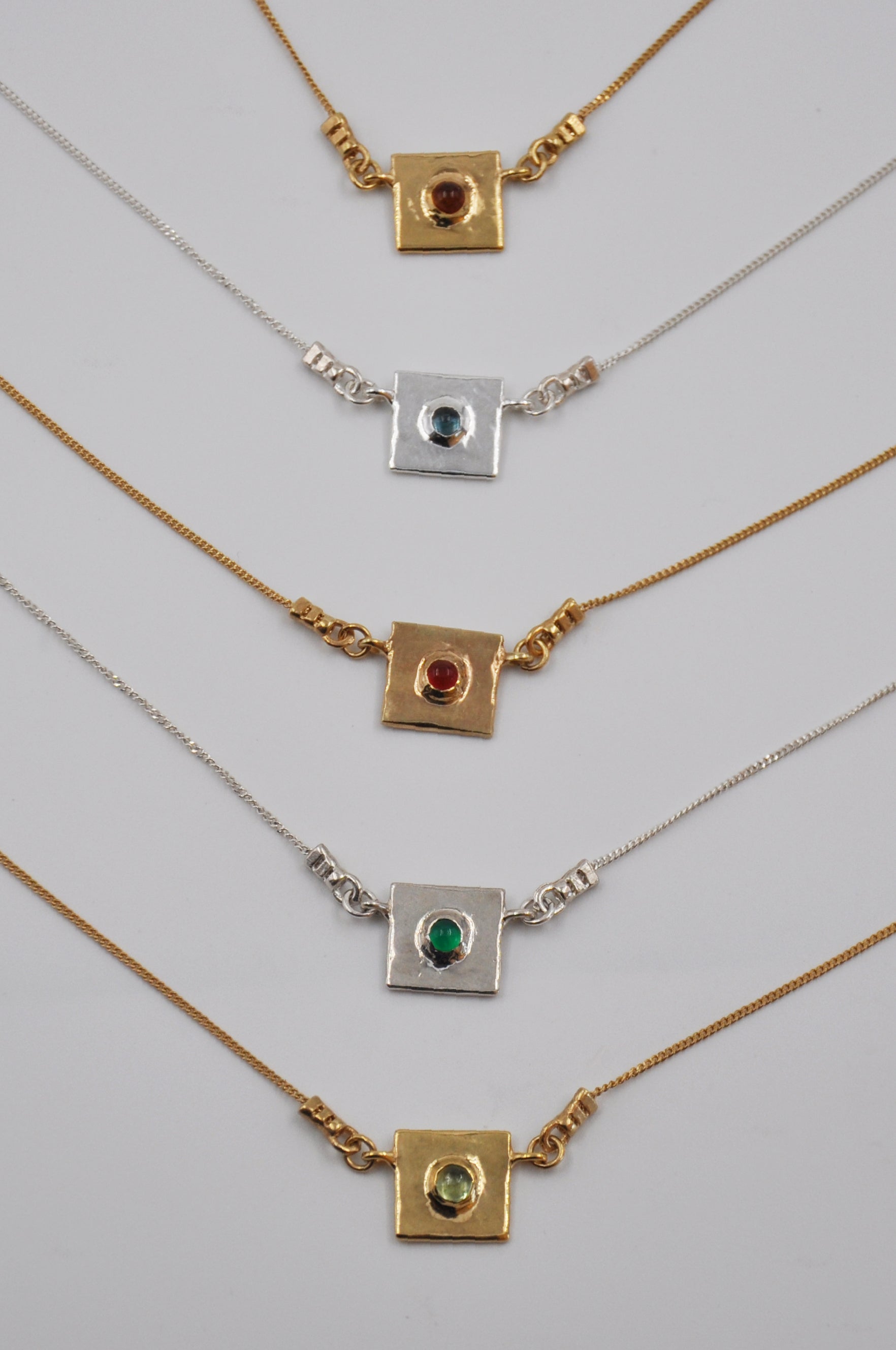 Set of gold and silver necklaces with gemstone pendants on a light gray background
