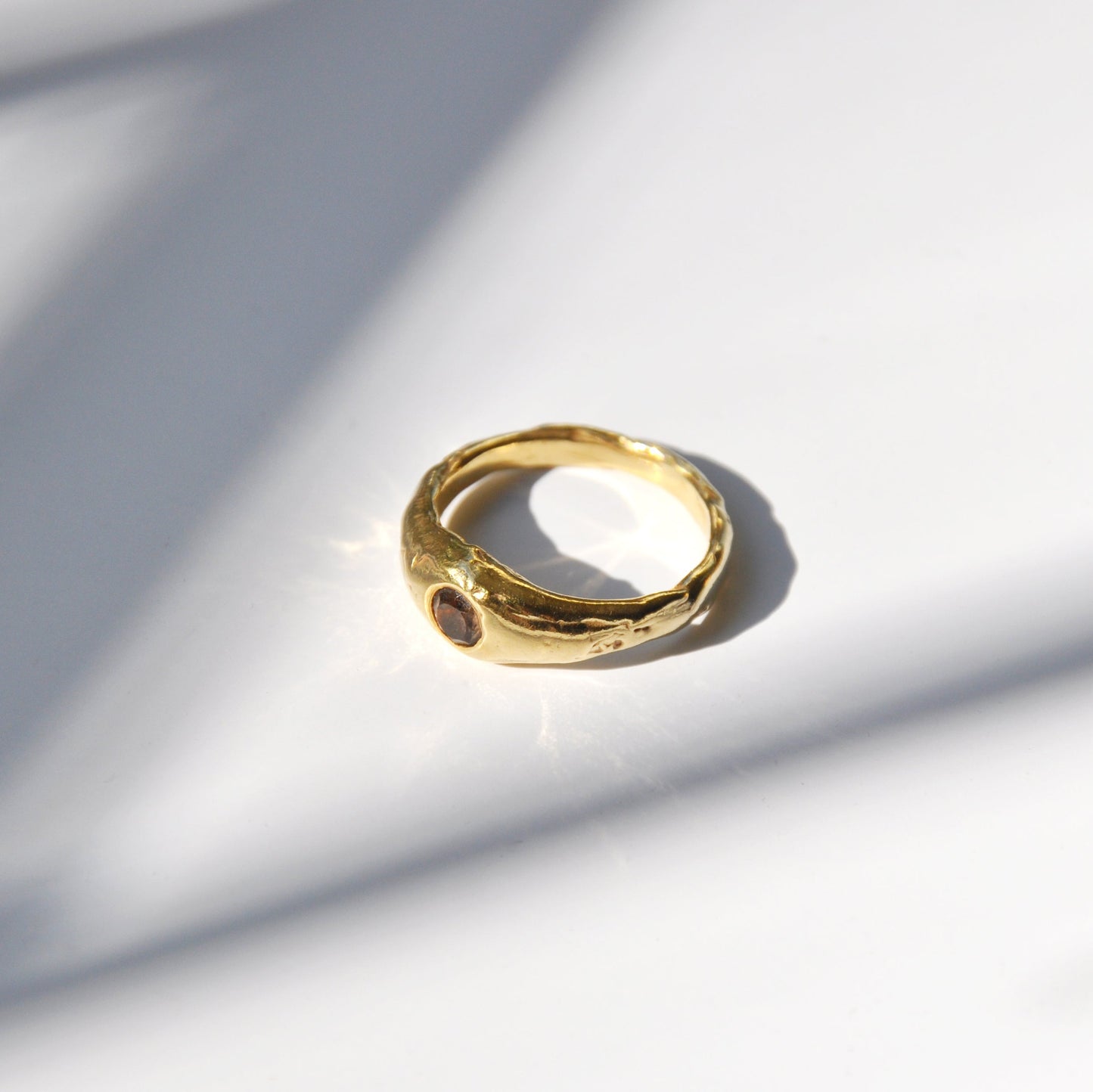 Gold ring on a light gray surface with soft shadows