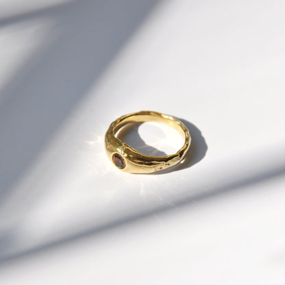 Gold ring on a light gray surface with soft shadows