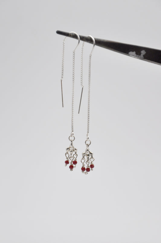 Silver earrings with red beads hanging from a stand on a light gray background