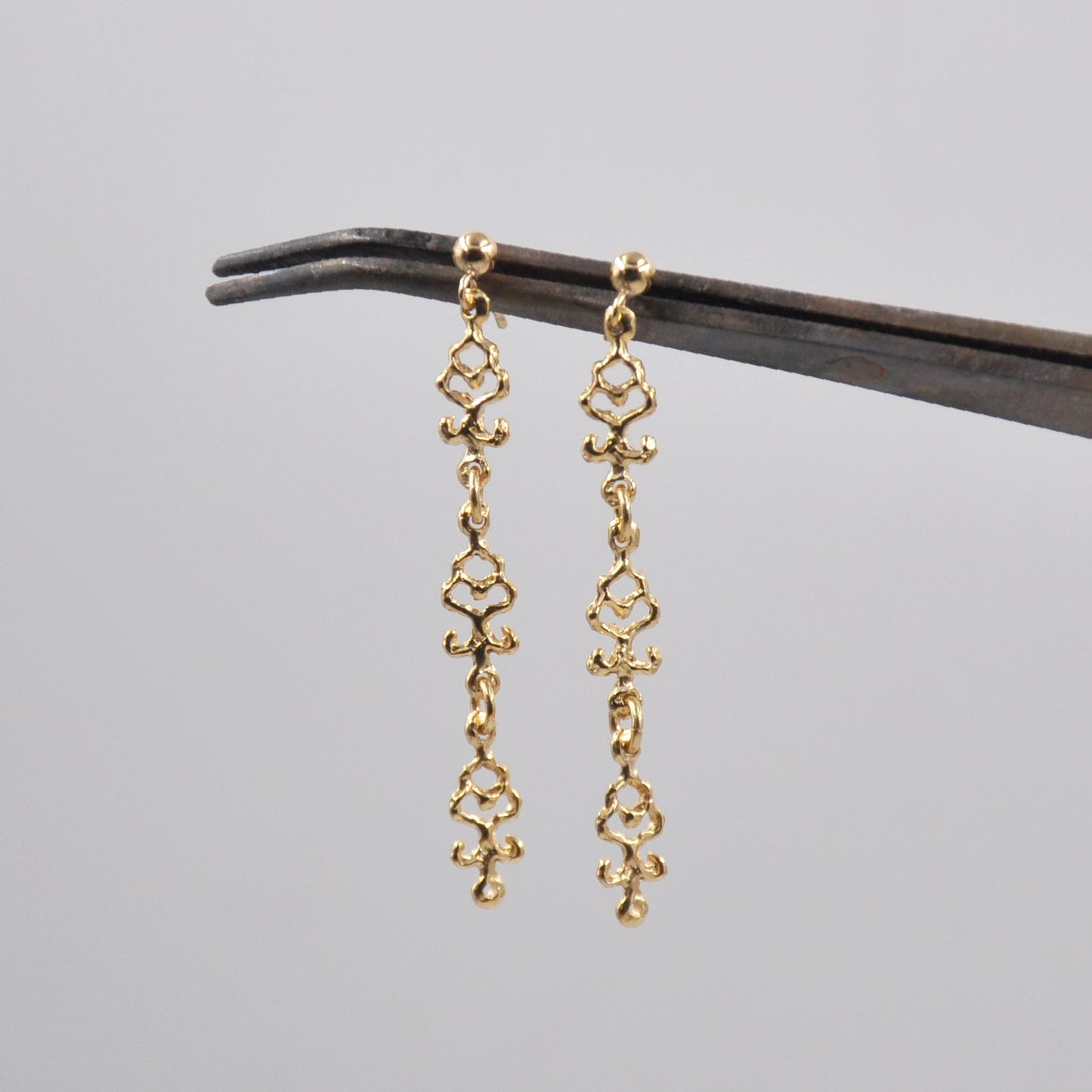 Gold earrings on a black stand against a gray background