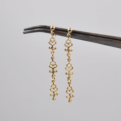 Gold earrings on a black stand against a gray background