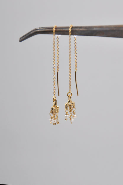 Gold earrings with dangling charms on a gray background