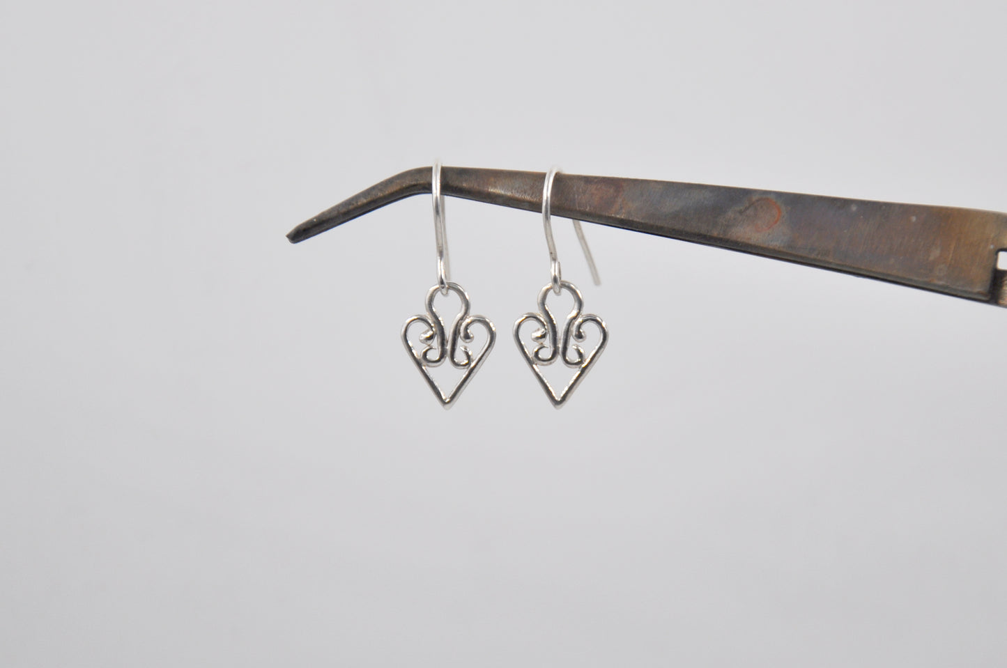 Heart-shaped silver earrings hanging on a wooden stick against a light gray background