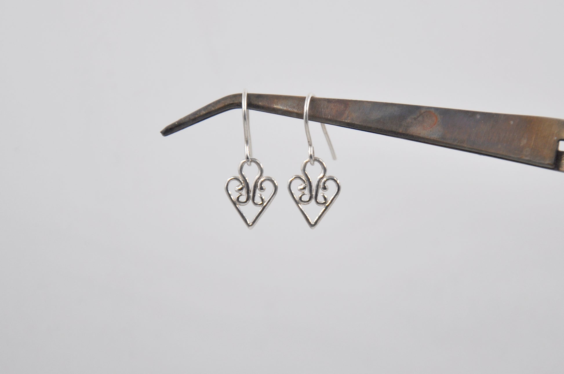 Heart-shaped silver earrings hanging on a wooden stick against a light gray background
