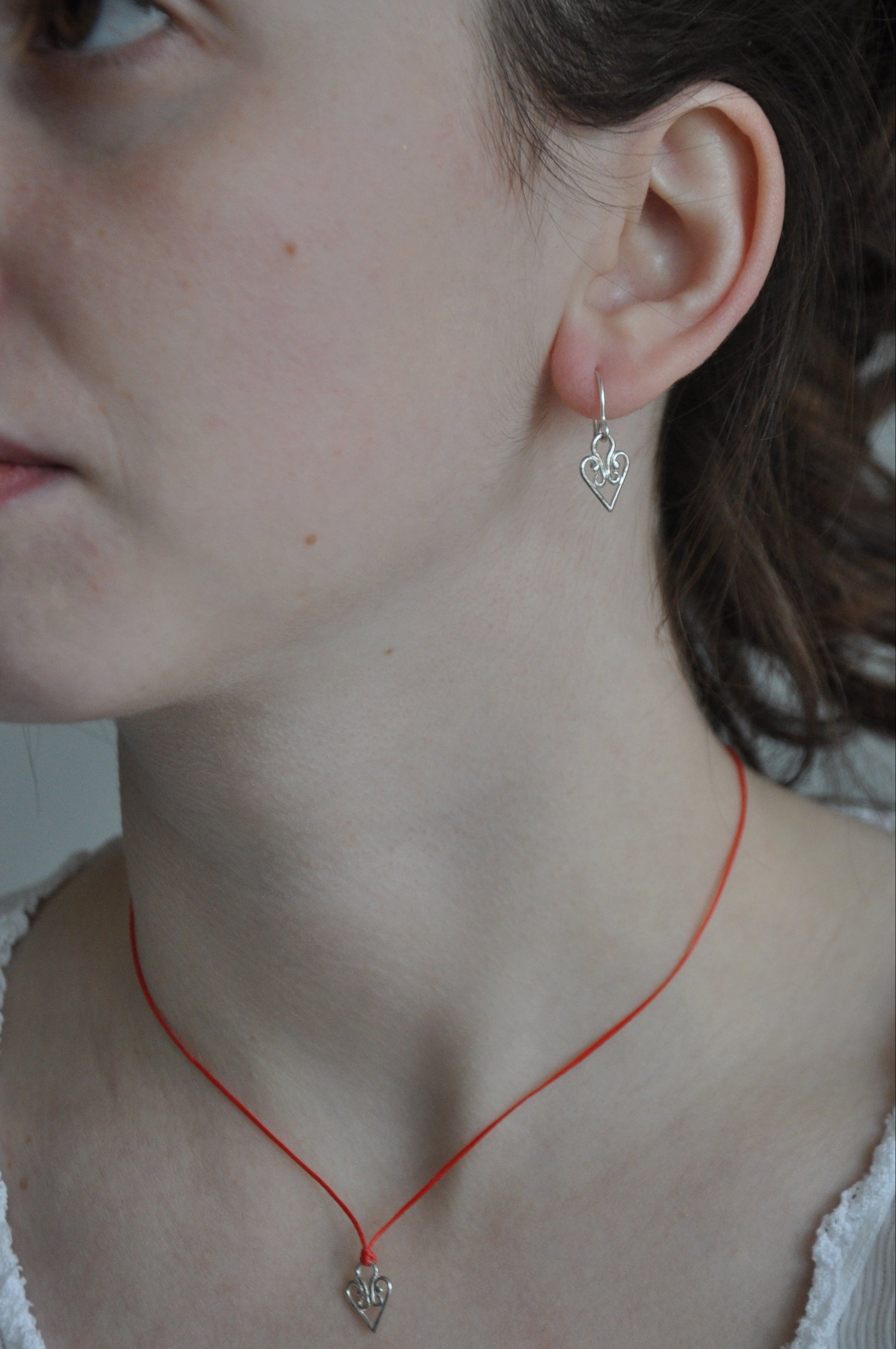 Close-up of a person wearing a red necklace and silver earrings.