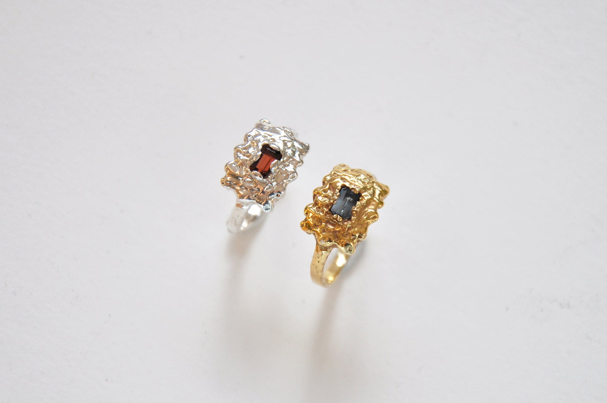 Two rings, one gold and one silver, with gemstones on a light gray background
