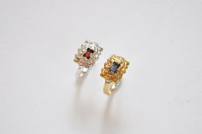 Two rings, one gold and one silver, with gemstones on a light gray background